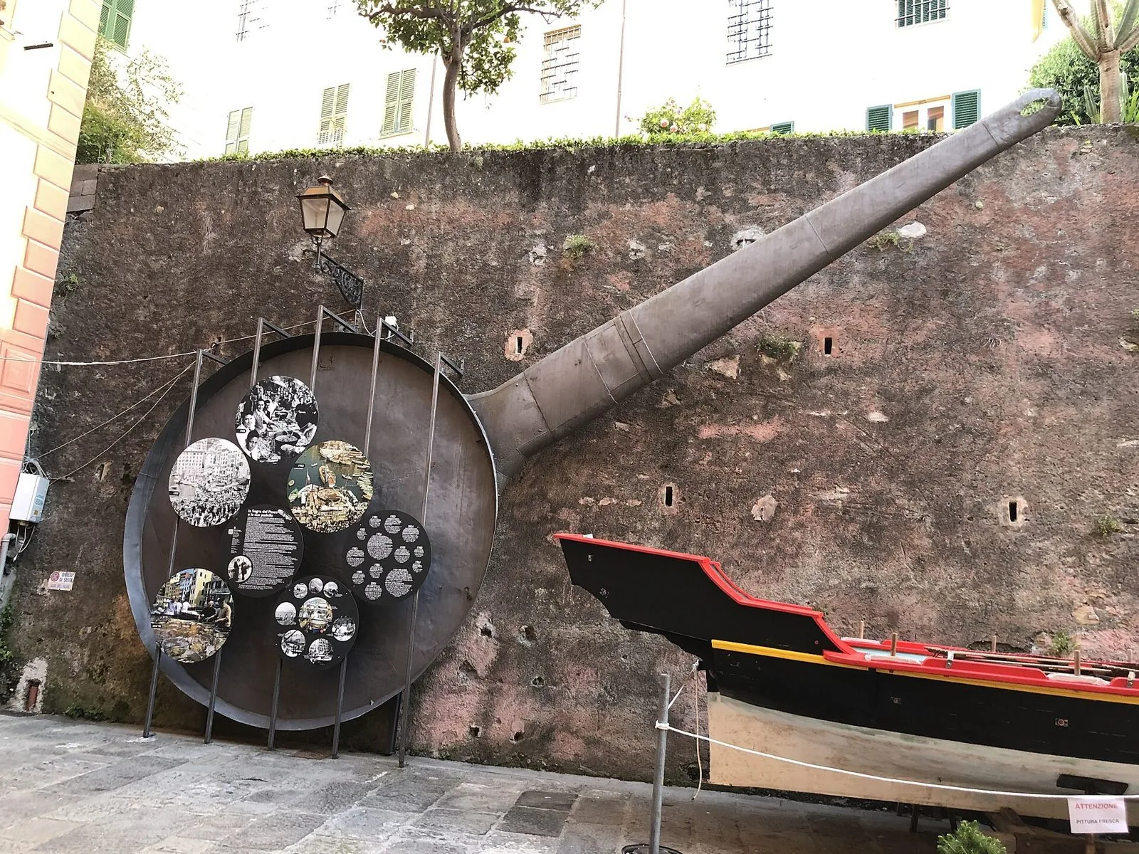 Una delle grandi padelle storiche della Sagra del Pesce esposta contro un muro in pietra a Camogli, accanto a una barca