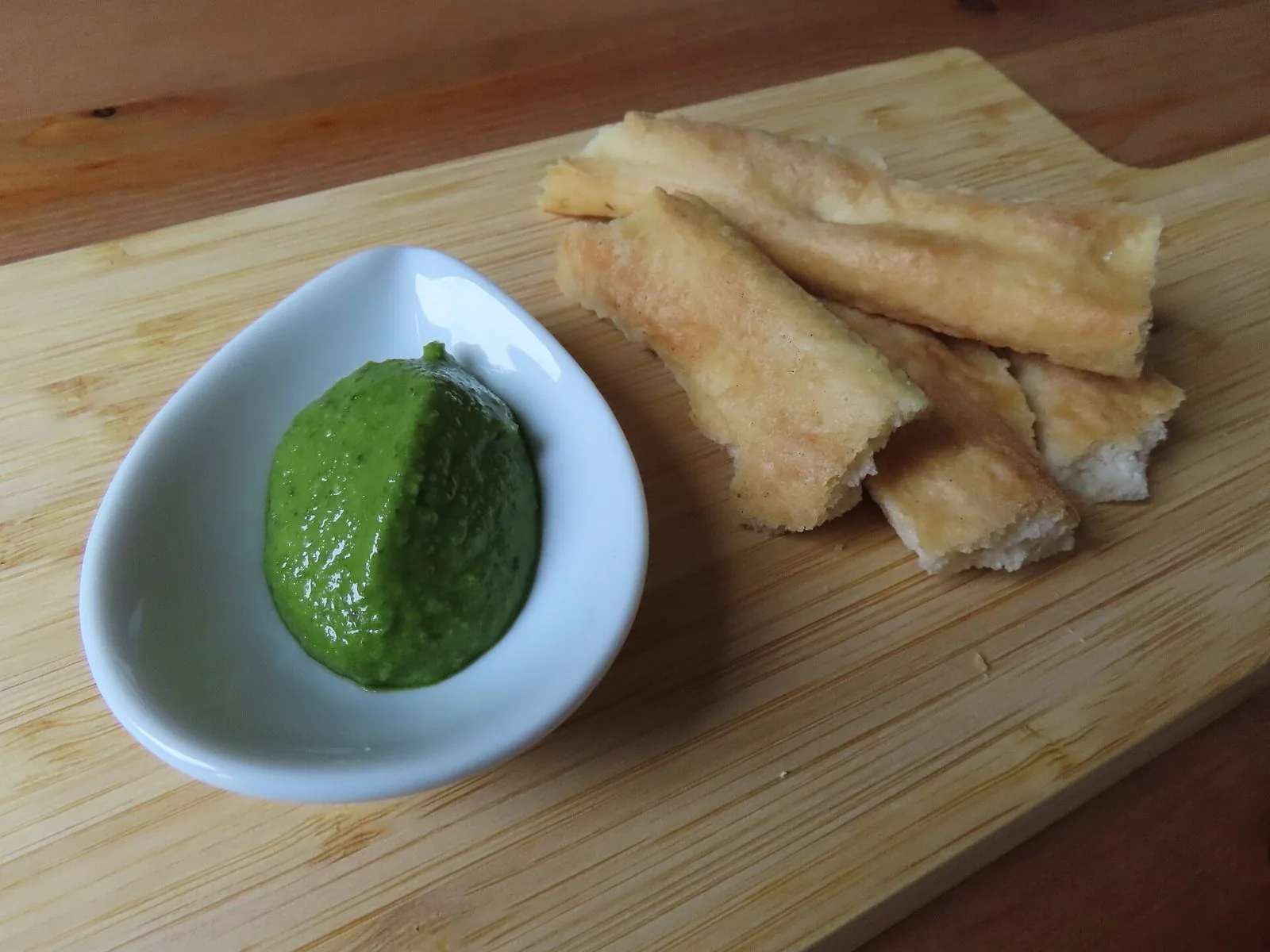 Ciotola di pesto genovese accanto a strisce di focaccia su un tagliere di legno