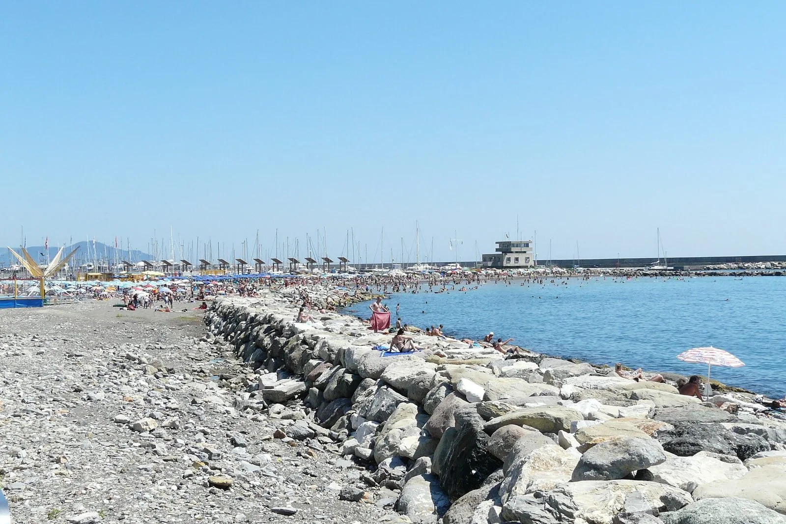 Spiaggia di Chiavari in estate con ombrelloni, scogliera e porto turistico sullo sfondo