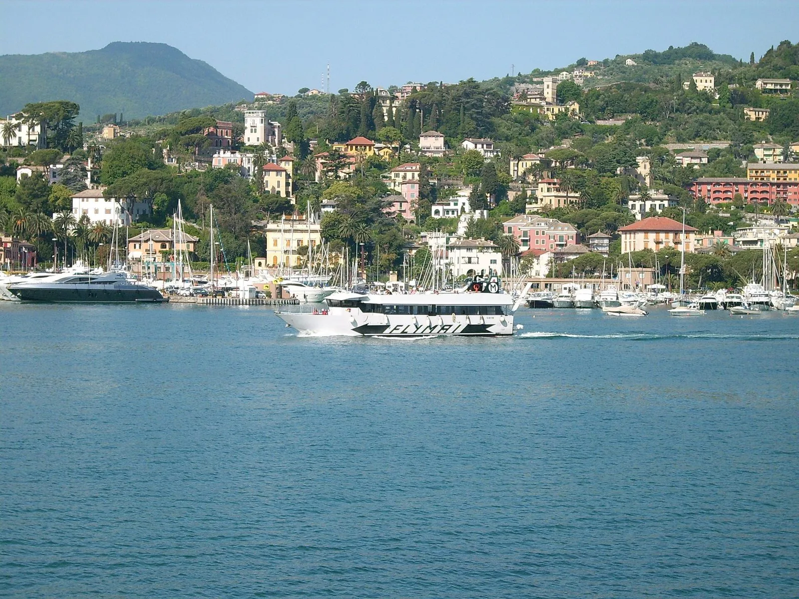 Battello passeggeri bianco che naviga nel Golfo del Tigullio davanti a un borgo con ville colorate e barche ormeggiate